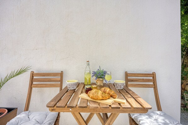 Une table en bois avec deux chaises, une bouteille, un bocal, un croissant et un verre de jus.