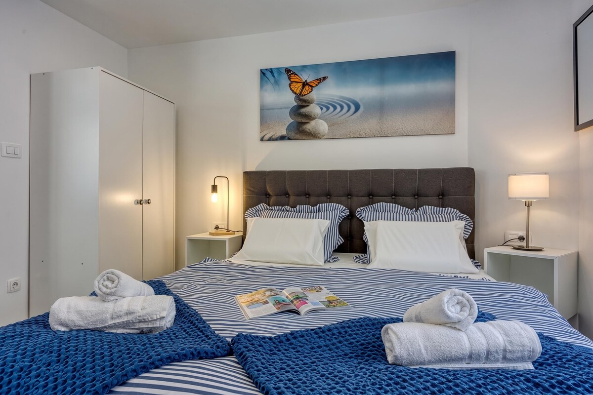 A hotel room with a bed, two bedside tables, a nightstand, a wardrobe, and a painting on the wall.