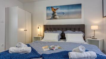 A hotel room with a bed, two bedside tables, a nightstand, a wardrobe, and a painting on the wall.