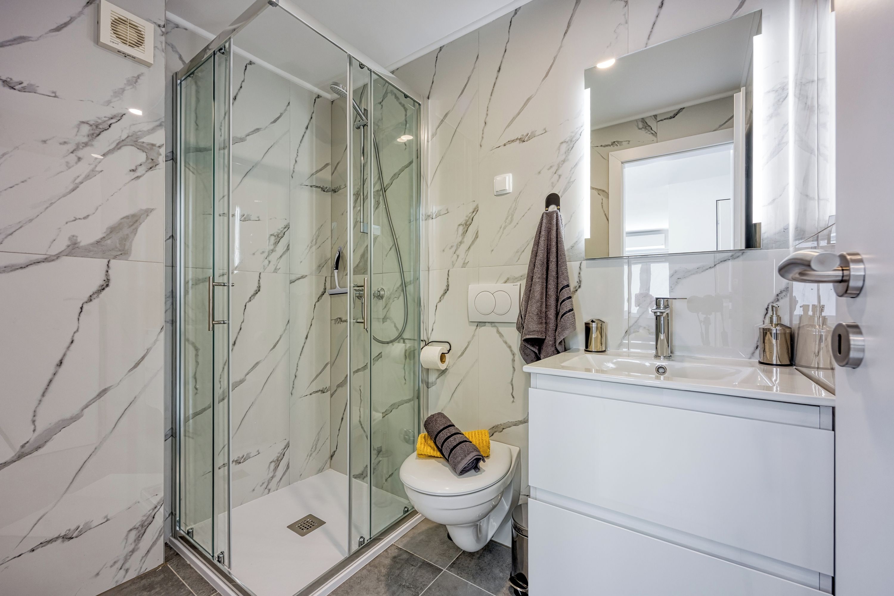 A modern bathroom with a glass-enclosed shower, a toilet, and a vanity with a mirror.