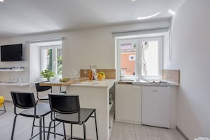 Una cocina moderna con lavavajillas integrado, un comedor con sillas negras y un televisor montado en la pared.