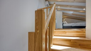 Escada de madeira que leva a um quarto com teto inclinado e uma cama.