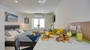 Un dormitorio moderno con cama, mesita de noche y una mesa con pan, fruta y bebidas.