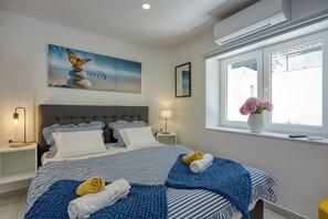Une chambre à coucher avec un lit, des oreillers, une table de chevet, une lampe, une fenêtre donnant sur un beau paysage et un tableau.