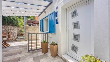 Un edificio residencial con fachada de piedra, una puerta blanca con amplias ventanas y un espacio exterior cubierto con mesa y sillas.