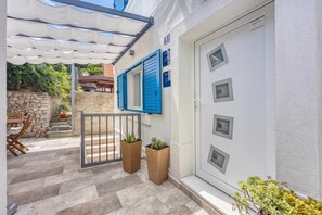 Un immeuble résidentiel à la façade en pierre, avec une porte blanche dotée de plusieurs fenêtres et un espace extérieur couvert comprenant une table et des chaises.
