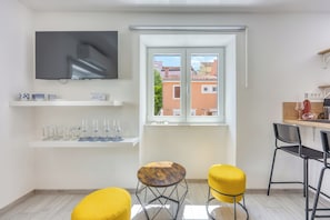 A modern kitchen with a TV, a window with a view of buildings, and two yellow stools.