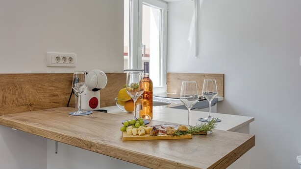 Un comptoir de cuisine avec un dessus en bois, un verre à vin, une bouteille d’huile d’olive et une planche à fromages avec divers accompagnements.