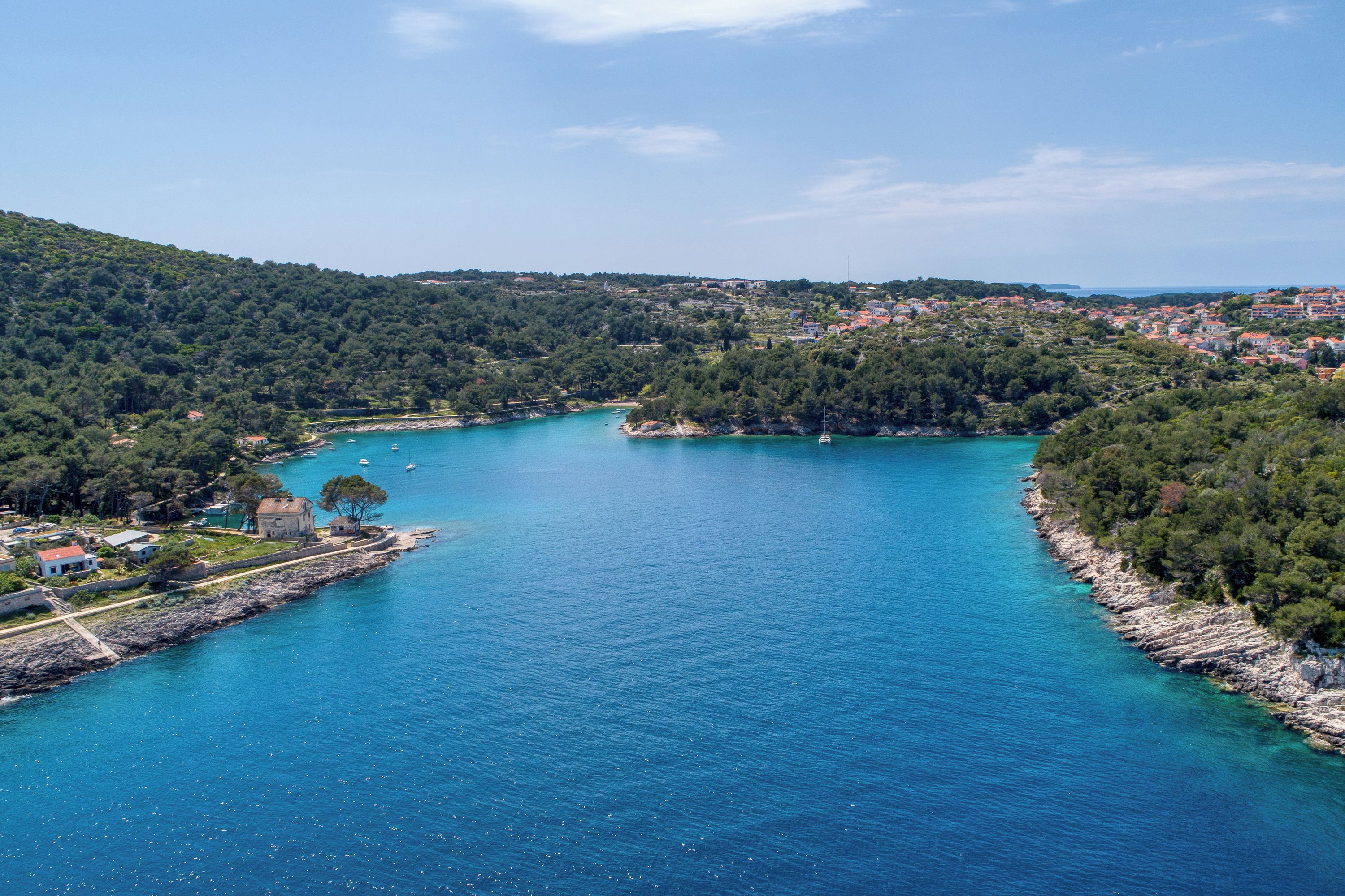 A coastal town with a clear blue sea, surrounded by hills and dense forests.