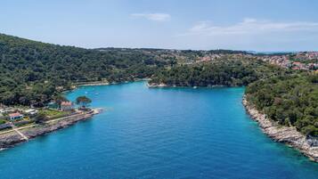 A coastal town with a clear blue sea, surrounded by hills and dense forests.