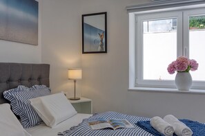 Une chambre d’hôtel avec un lit, une table de chevet avec une lampe, un tableau encadré au mur et une fenêtre donnant sur l’extérieur.