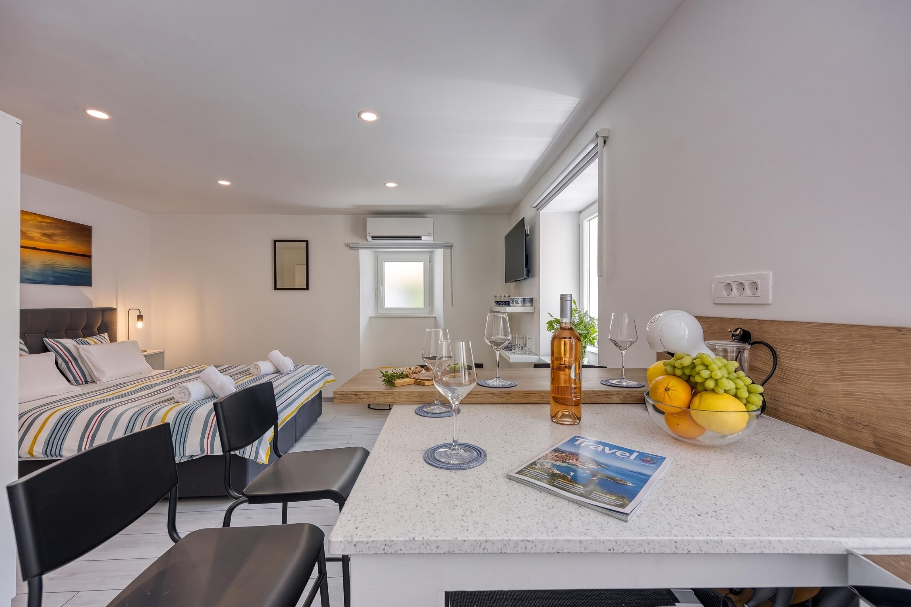 A modern hotel room with a bed, a small dining area, a kitchen, and a living area.