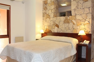 A hotel room with a stone wall, a bed with a white quilt, two bedside lamps, and a phone on the nightstand.