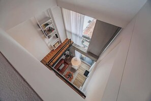 Una habitació ampla amb sostre alçat, terra de fusta, un sofà, una taula de dinar i una biblioteca.