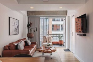 Un salon moderne avec un canapé en cuir, une table basse en bois et un téléviseur fixé au mur.