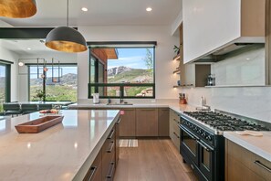 A modern kitchen with a large island, a gas stove, and a view of a mountainous landscape. - NEW! 1868 W SkyRidge Drive 4 Bedroom Home with Hot Tub by Deer Valley Resort (Daniel)