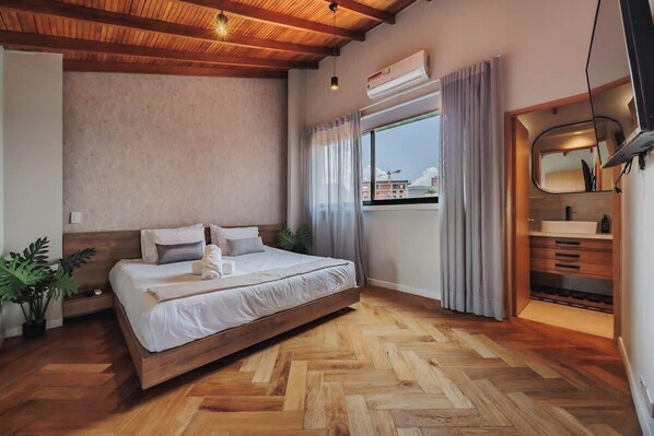 Ein modernes Schlafzimmer mit Holzboden, einem großen Bett, einem Fenster mit Vorhängen und einem eingebauten Schminktisch mit Spiegel.