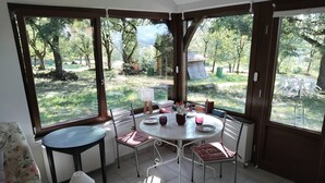 A room with a round table, chairs, and a view of a garden through large windows. - PAULAGITE for 2 to 4 people, view of the Dordogne, near Padirac and Rocamadour (Gintrac)