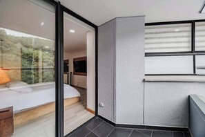 A modern bedroom with a glass door leading to a balcony, a bed, and a small seating area.