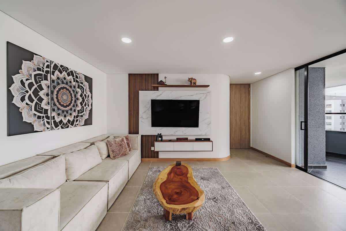 Uma sala de estar moderna com sofá, uma mesa de centro de madeira única, uma grande obra de arte na parede, uma televisão de tela plana e lareira.
