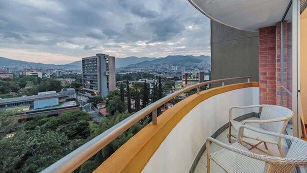 A balcony with wicker chairs, a view of a cityscape, and a cloudy sky. - |EP| Well Located Apt w/Fast Internet,Balcony,Pool (Medellín)