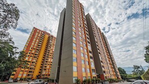 A high-rise residential building with multiple balconies, a parking area, and a clear sky. - |EP| Well Located Apt w/Fast Internet,Balcony,Pool (Medellín)