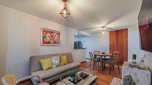 A living room with a sofa, a coffee table, and a dining area with chairs and a table. - |EP| Well Located Apt w/Fast Internet,Balcony,Pool (Medellín)