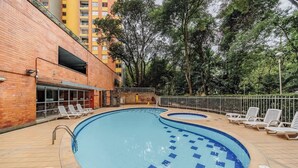 A swimming pool with a tiled deck, surrounded by lounge chairs and a brick building. - |EP| Well Located Apt w/Fast Internet,Balcony,Pool (Medellín)