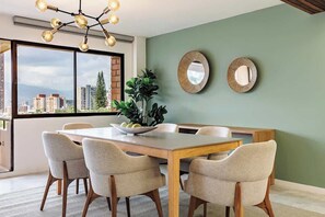 Un comedor con una mesa, sillas, una planta y dos espejos en la pared.
