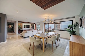 Una sala de estar moderna con una mesa de comedor de madera, sofás color beige y un ventanal con vistas a la ciudad.