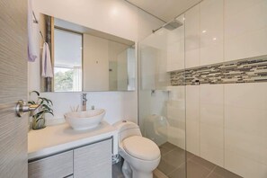 A modern bathroom with a white sink, a toilet, and a glass shower enclosure.