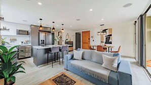 A modern living room with a sofa, coffee table, and kitchen area with a dining table and chairs. - |EP| 2BR/W City Views Apt w/Office (Medellín)