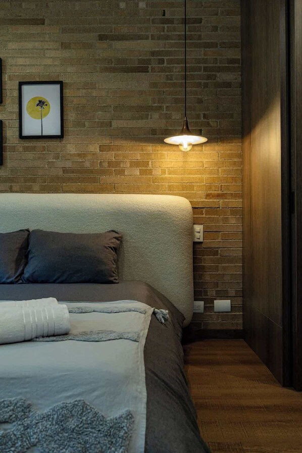 A modern bedroom with a brick wall, a hanging light fixture, and a bed with a grey and brown duvet.