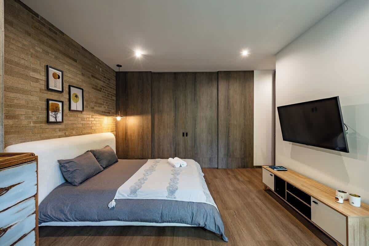 A modern bedroom with a large bed, wooden panel walls, a flat-screen TV, and a built-in TV stand.