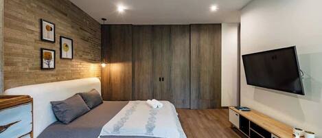 A modern bedroom with a large bed, wooden panel walls, a flat-screen TV, and a built-in TV stand.