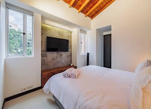 Ein Schlafzimmer mit einem großen Bett, einem flachbildfernseher an der Wand und einem Fenster mit Blick ins Freie.