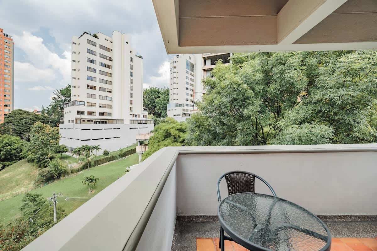A balcony with a glass table and chairs, overlooking a garden and tall buildings.