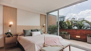 Un dormitorio moderno con una cama grande, mesitas de noche y vistas a la ciudad a través de amplias ventanas.
