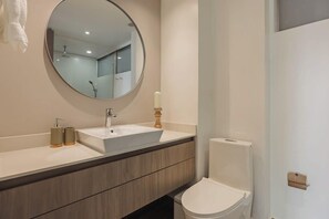 A modern bathroom with a round mirror, a white sink, a wooden vanity, and a white toilet.