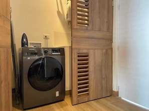 A compact, modern laundry room with a front-loading washing machine, a dryer, and a wooden cabinet with ventilation slats.