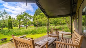 Een overdekt terras met houten meubels en uitzicht op een weelderige tuin.