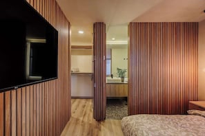 Habitación de hotel con pared de paneles de madera, televisor de pantalla plana, cama con ropa de cama estampada y baño con lavamanos y espejo.