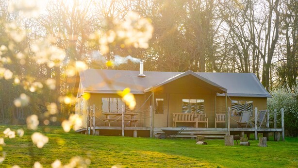 A cabin with a porch, outdoor seating, and a wheelbarrow. - Dog Friendly Safari Tent, Skylark at Sweffling Hall, Suffolk (Sweffling)