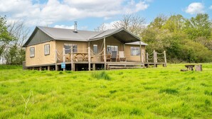 A two-story house with a porch, surrounded by a grassy field and trees. - Dog Friendly Safari Tent, Skylark at Sweffling Hall, Suffolk (Sweffling)
