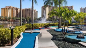 A landscaped pool area with a fountain, palm trees, and a view of high-rise buildings in the background.