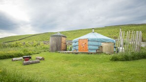 A yurt with a wooden door and a blue tarp, surrounded by logs and a wooden structure. - Lapwing Yurt, Askrigg (Askrigg)