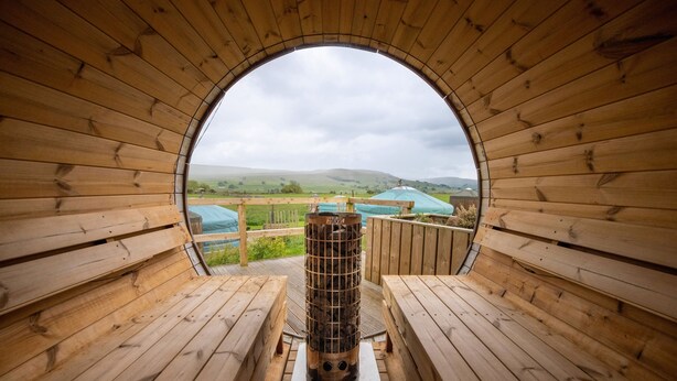 A wooden structure with a circular opening, benches, and a view of green fields and distant buildings. - Lapwing Yurt, Askrigg (Askrigg)
