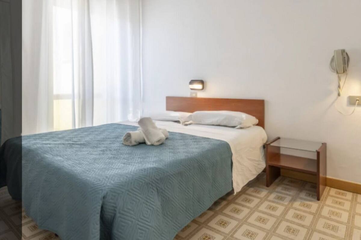 A hotel room with a bed, a bedside table, and a wall-mounted light fixture.