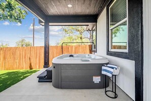 A hot tub in a covered outdoor area with a wooden fence and a concrete patio.