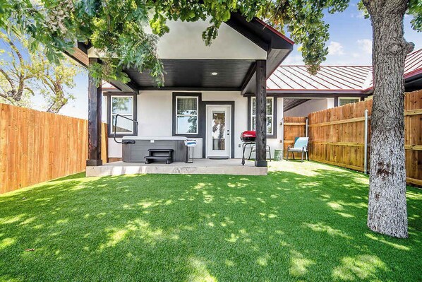A backyard with a covered patio, a grill, and a wooden fence.